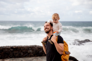 A Father Learning to be Content Carries His Child on His Shoulders By the Sea